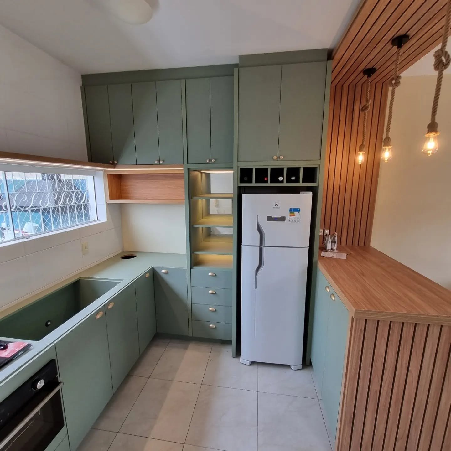Cozinha verde eucalipto com bancada de madeira e iluminação